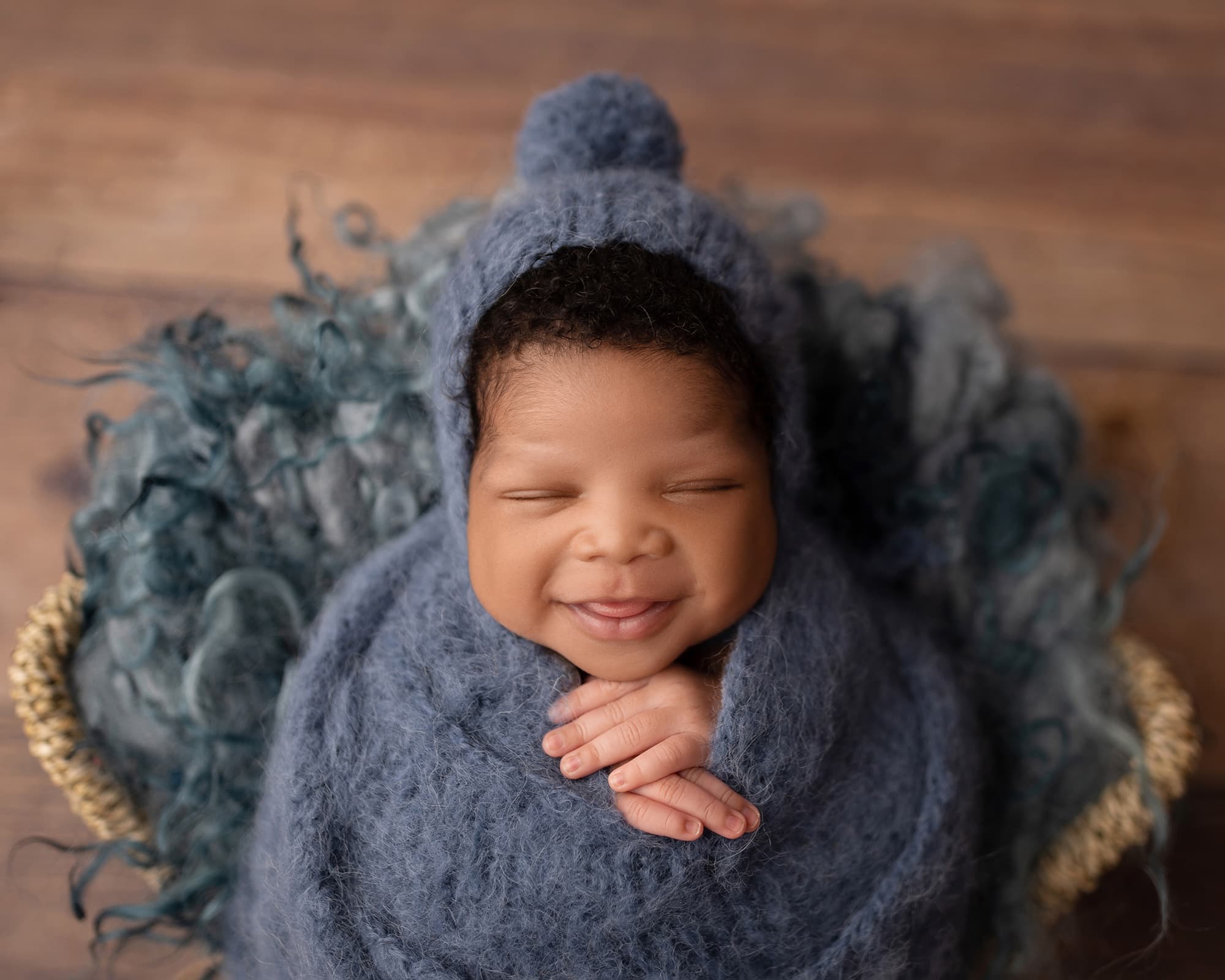 A smiling newborn baby wrapped in a blue fuzzy blanket and bonnet