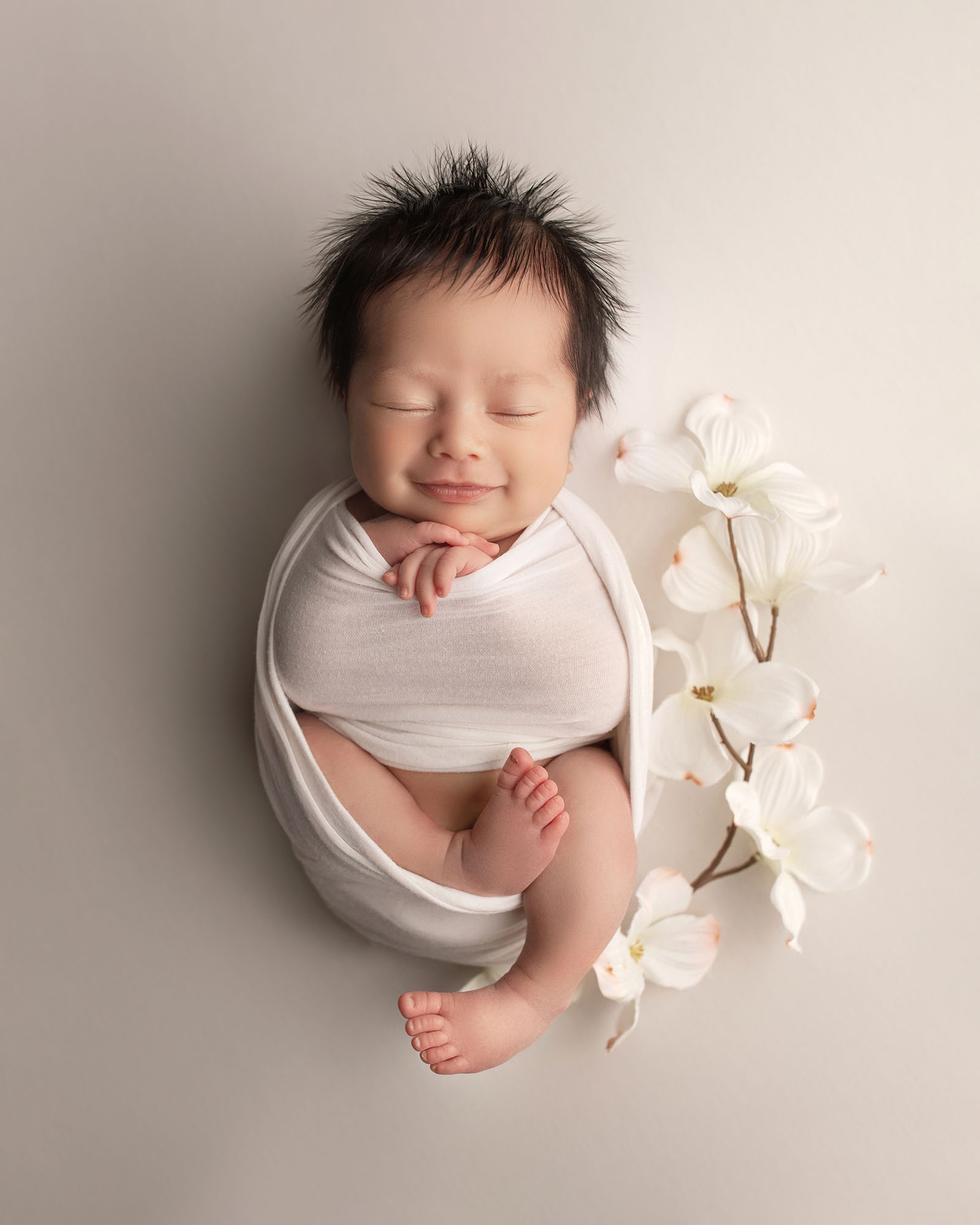 Newborn baby smiling and is in a white wrap.
